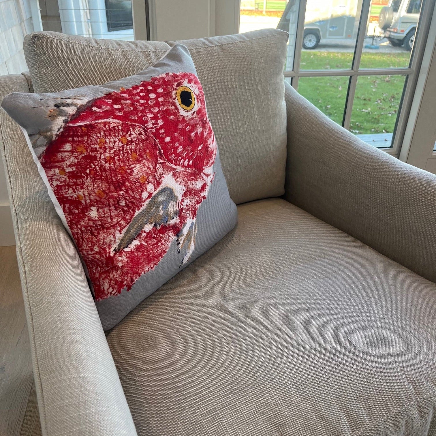 Red fish pillow on a beige sofa with a window in the background